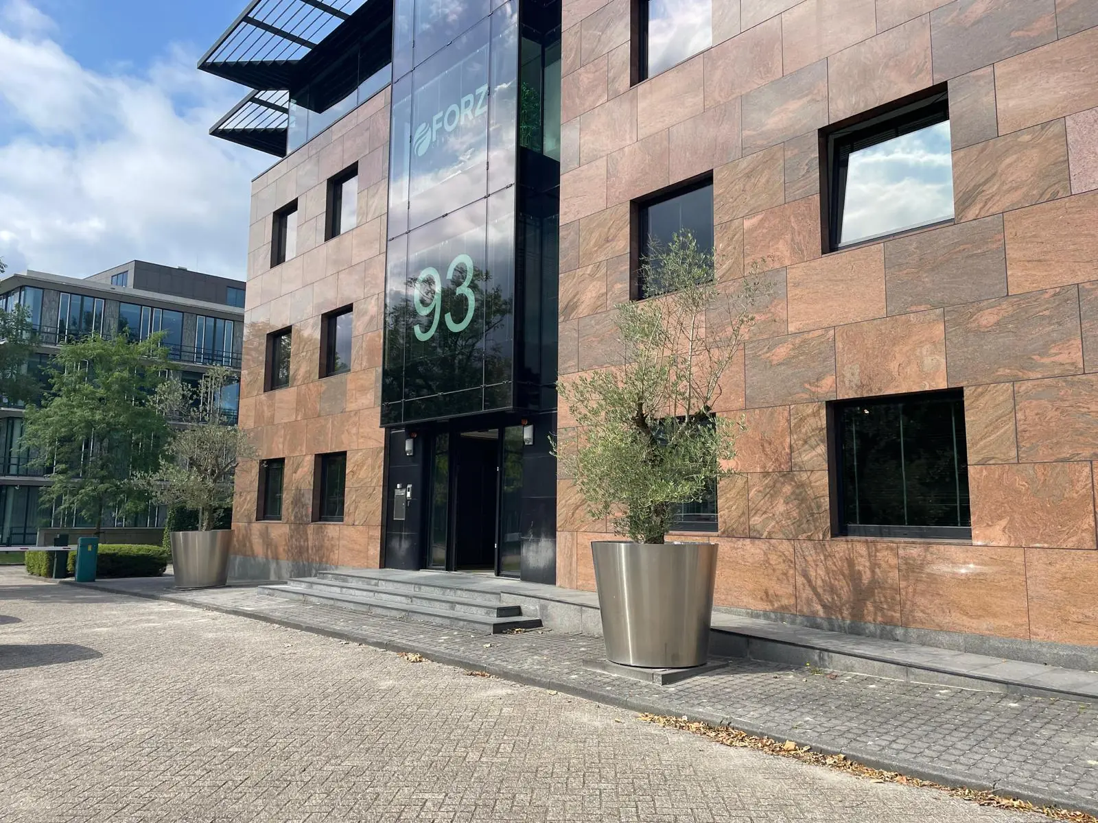 Modern kantoorgebouw aan de De Cuserstraat 93 met gevel van natuursteen en grote plantenbakken bij de entree.